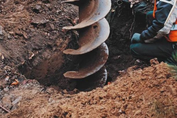 Skilled Construction Worker in Protective Vest Overseeing Big Earthworks Machine Drill Excavating Ground